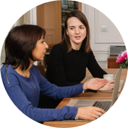 Twee vrouwen zitten aan een tafel en kijken naar een laptop.