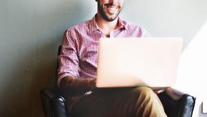 Man in checkered shirt sitting on chair and holding laptop