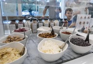A shot of nine bowls of varied toppings at Pressed with customers onlooking