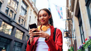 A woman walking outside, taking off her headphones and using her mobile phone