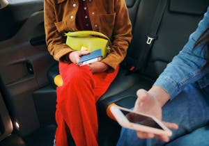Woman sitting in the back of a car, holding a book and phone