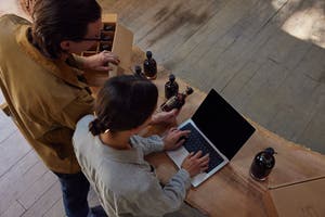 Two individuals looking at a laptop device while packaging products.