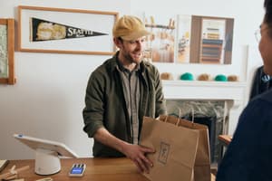 An action shot of a store clerk handing a bag to a customer, accentuating the topic of how to start a retail business.