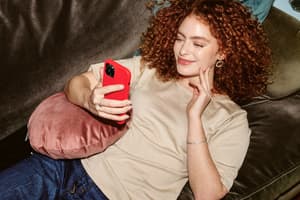 Woman smiling on her phone as she lies on the couch.