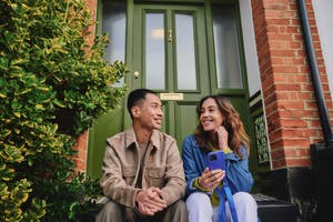 Couple sitting on front steps, smiling, woman holding a phone