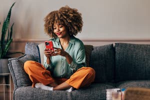 Customer sits on a coach and uses AI on their phone as part of their online shopping journey.