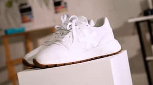 Weiße Sneaker mit brauner Sohle stehen auf einem weißen Podest in einem hellen Raum.