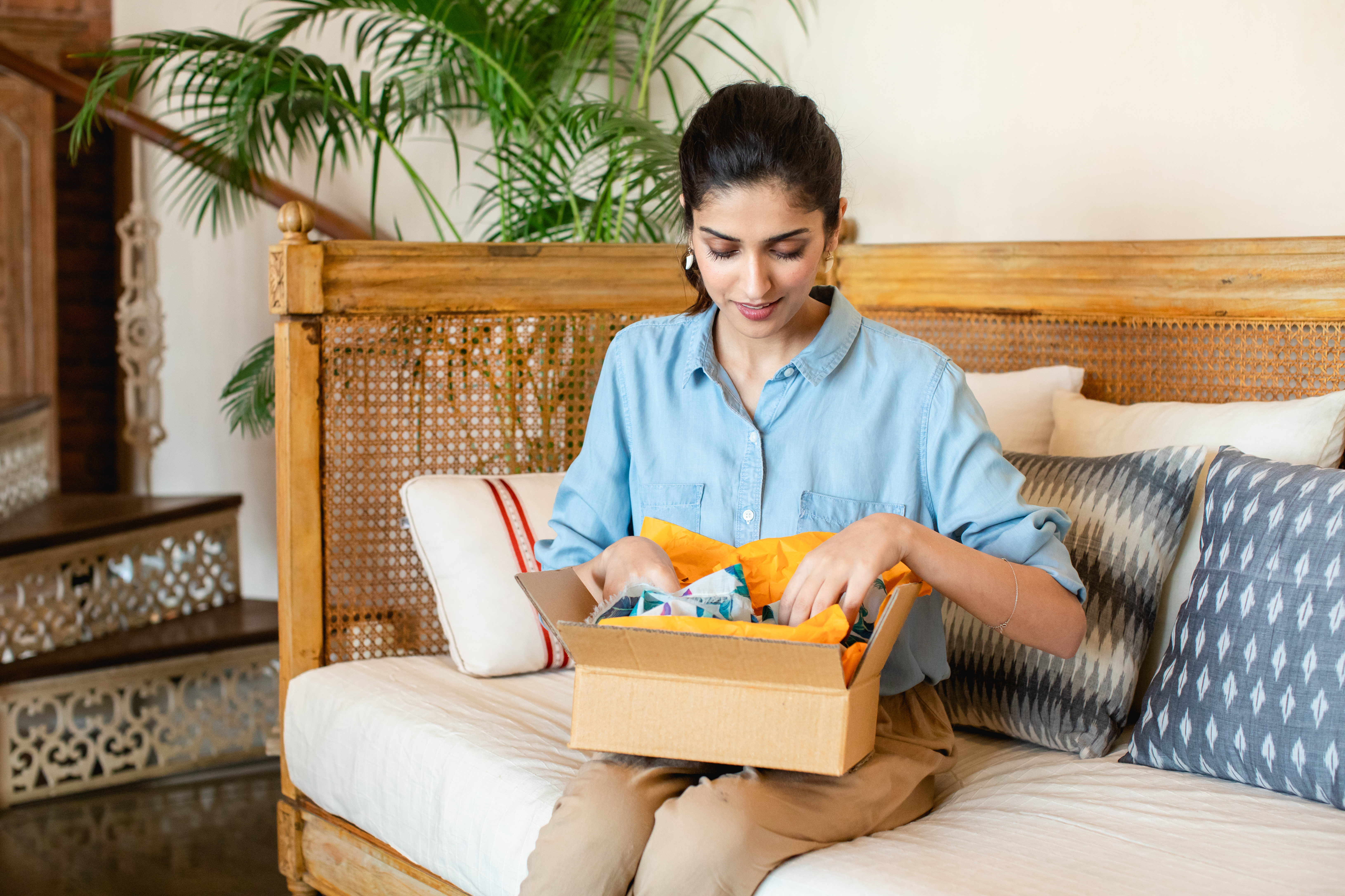 Woman sitting on couch opening up a package of goods in a cardboard box