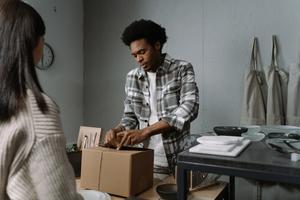 Man in gray flannel wrapping a cardboard package for a customer standing in front of him