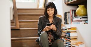 Woman sitting on stairs surrounded by books and using her phone