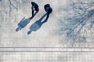 Bird's eye view shot of two men in business suits walking on pavement and their shadows