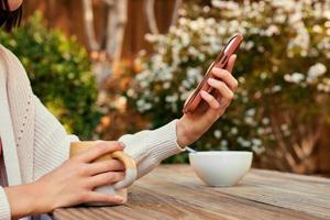 Person sitting at a table with one hand holding a mug and the other holding a smartphone.