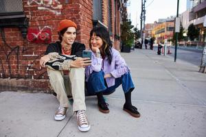 Two trendy young people share a moment looking at a phone on a city street corner.