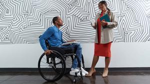 Employee in wheelchair talks to coworker standing in front of a black and white designed wall