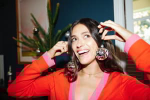 A woman holding up two Christmas ornaments and smiling.