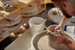 Eine Person mit Bart, die von zu Hause aus Geld verdient, indem sie einen Tontopf auf einer Töpferscheibe formt.