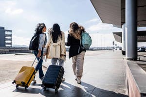 Three women carry luggage inside of an airport to take a flight.