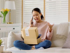 Female customer with an opened box on her lap filing a purchase claim on the phone
