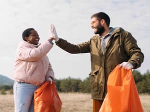 Deux personnes en manteau d'hiver ramassant des ordures dans un champ, un exemple d'association caritative à laquelle vous pouvez faire un don avec PayPal