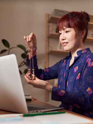 A woman holds up a necklace to her webcam, illustrating how you can sell goods and services online with PayPal 