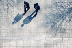 Bird's eye view shot of two men in business suits walking on pavement and their shadows
