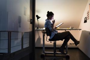 Woman sitting at desk at night looking at a notepad