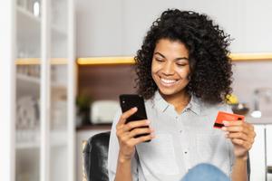 Smiling young woman entering bank card details into her phone