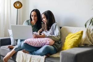 Woman working from home on her laptop with preteen daughter next to her