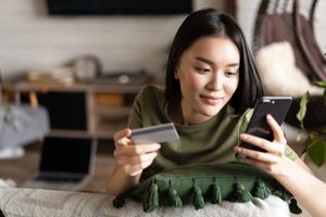 Young asian woman buying from online shop at home using mobile phone and credit card