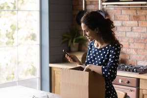 Woman unboxing a package in her home while also holding a phone in her hand