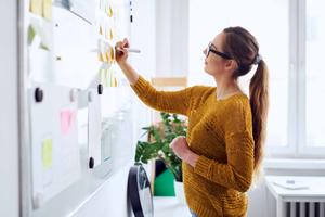 Young businesswoman in yellow sweater planning on whiteboard in startup office
