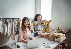 Two women putting clothing in boxes at a white desk
