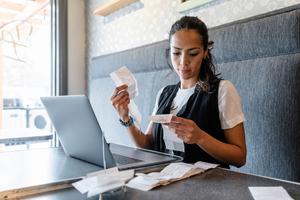 Female business owner reviewing receipts at laptop in cafe