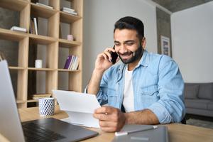Man sitting at a desk on the phone looking at a piece of paper