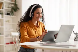 Mujer sonriente con auriculares usando su tablet y computadora en la oficina.