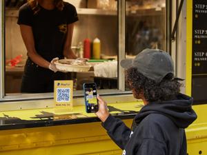 A guy scanning a PayPal QR code in front of a food truck to pay for his meal.
