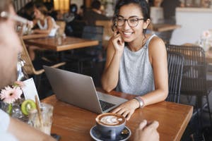 A woman in a coffee shop doing her small business accounting on her laptop.