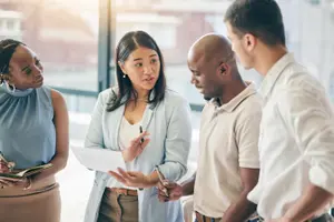 Four business professionals in discussion, reviewing documents together in an office setting.