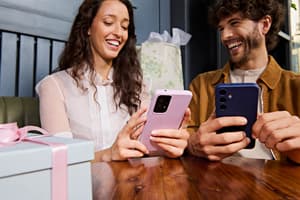 Two customers laughing while shopping on their smartphones, illustrating cross-border e-commerce trends as consumers browse and purchase from international retailers online.