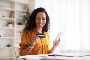 A lady smiling at her bank card while holding a mobile phone