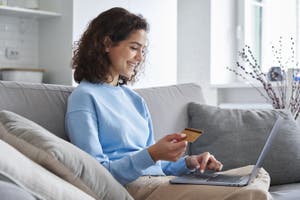 A women holds a credit card, finalizing an online purchase on her laptop and looking at the checkout page.