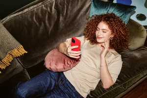 A smiling customer lays on a green couch while making a credit card purchase online, showing how smoother payments can reduce international cart abandonment. 