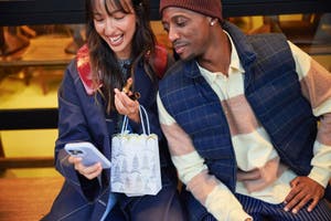 A couple shops for holiday gifts on a phone.