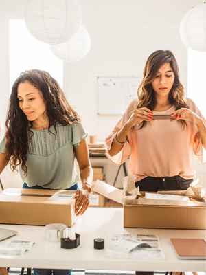 Deux femmes d'affaires occupées à emballer des articles et à vérifier les commandes, illustrant une entreprise qui grandit avec PayPal