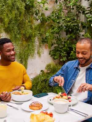 3 amigos hablando alegremente durante una comida, mostrando un ejemplo de personas que confían en PayPal para enviar, gastar y administrar su dinero