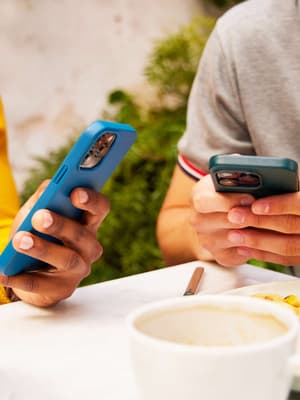 Deux personnes assises à une table et utilisant leur smartphone pour envoyer et recevoir de l'argent, illustrant l'une des nombreuses façons d'utiliser PayPal