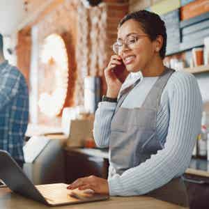 Femme au téléphone derrière un comptoir, utilisant un ordinateur portable