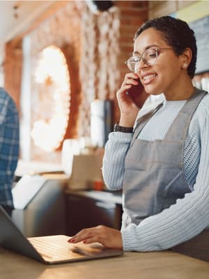 Woman on the phone behind a counter using a laptop