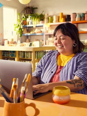 A female business-owner works on her laptop in the middle of a store.