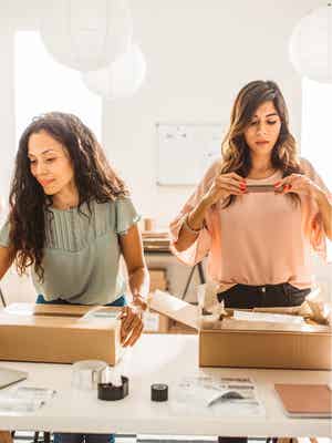 Zwei vielbeschäftigte Geschäftsfrauen, die Artikel verpacken und Bestellungen prüfen – ein Beispiel für ein Unternehmen, das mit PayPal wächst